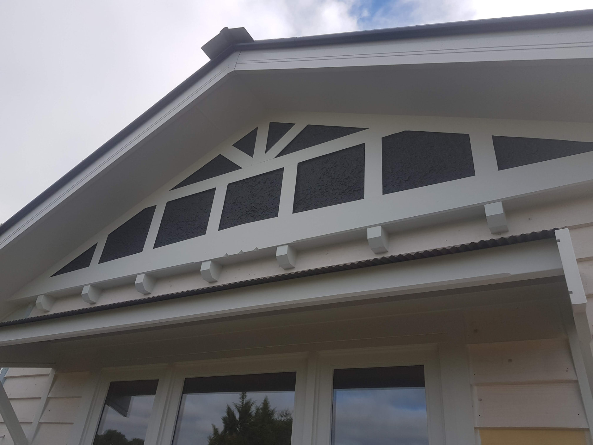 Dark stucco-rendered gable end with white decorative timber brackets and contrasting fascia on a Melbourne home exterior