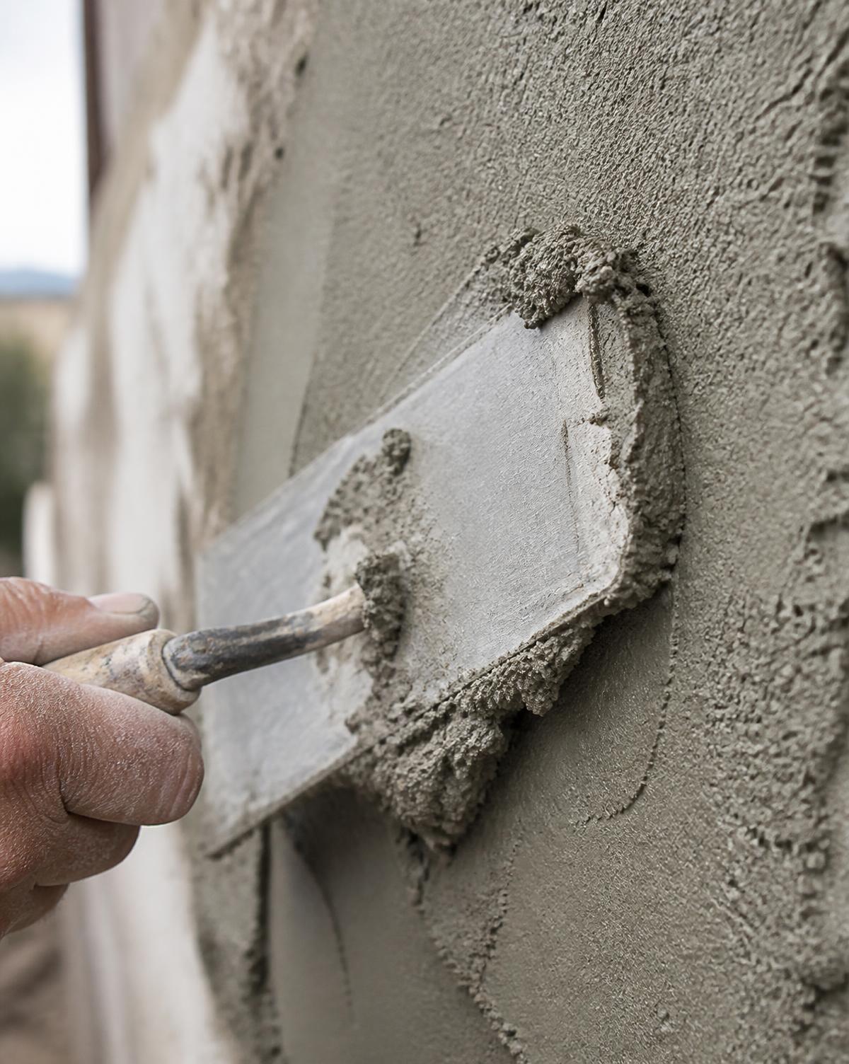 Steel trowel spreading fresh cement render across a wall